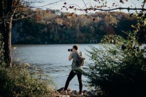 Man with Backpack Taking Picture Beside Lake